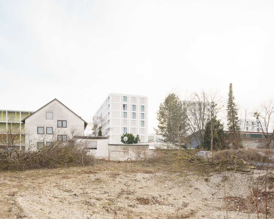 Brachfläche im Vordergrund mit Einfamilienhaus als Altbestand, Neubauten im Hintergrund